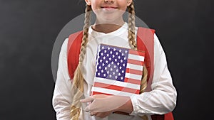 Smiling schoolgirl holding book with USA flag, English language studying