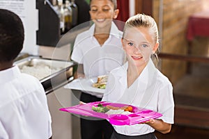 Smiling schoolgirl holding food tray in school cafeteria