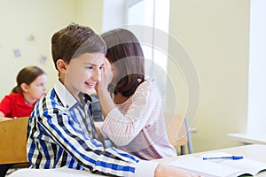 Smiling schoolgirl whispering to classmate ear