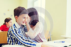 Smiling schoolgirl whispering to classmate ear