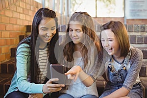 Smiling schoolgirls sitting on the staircase using mobile phone