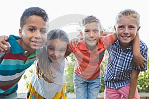 Smiling schoolkids standing with arms around in campus