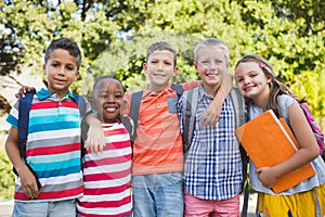 Smiling schoolkids standing with arms around in campus