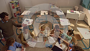 Smiling schoolteacher explaining lesson to students at round table