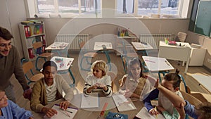 Smiling schoolteacher explaining lesson to students at round table