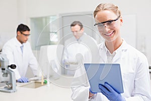 Smiling scientist using tablet while colleagues working behind