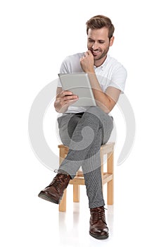 Smiling seated man thinks while reads on his tablet