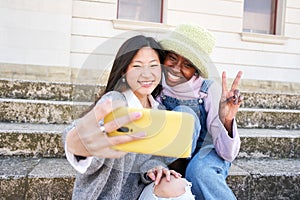 Smiling selfie of Two cheerful female friends having fun. Interracial Couple taking picture with smart mobile