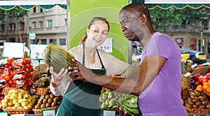 Smiling seller woman is helping man choose melone in the fruit market.