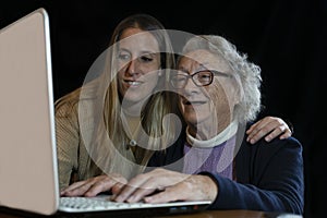 Smiling senior 80s woman with granddaughter using computer.Young female help or teach to surf internet grandparent.Family having