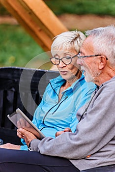 Smiling senior active couple sitting on the bench looking at tablet computer