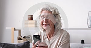 Smiling senior adult grandmother using smart phone sitting on sofa