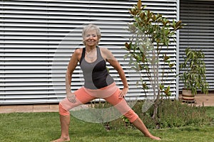 Smiling senior blond woman doing her stretches in the garden