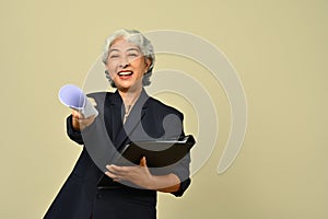 Smiling senior businesswoman wearing black suit and eyeglasses posing isolated on beige background