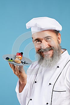Smiling Senior Chef Holding Dessert on Blue