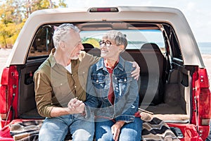 smiling senior couple embracing and looking at each other near car.