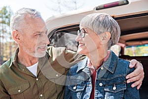 smiling senior couple embracing and looking at each other near car.