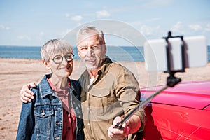 smiling senior couple embracing and taking selfie in sunny day.