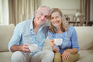 Smiling senior couple holding cup of coffee in living room