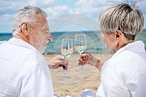 smiling senior couple holding wine glasses with wine and looking at each other at beach.