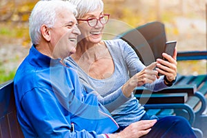 Smiling senior couple jogging in the park using smartphone