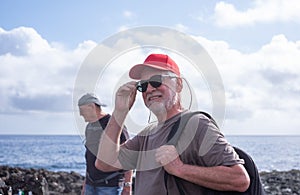 Smiling senior couple of men walking in the nature of Malpais de Guimar at Tenerife island with backpack on shoulder, horizon over photo