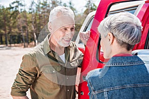 smiling senior couple standing near red car and looking at each other.