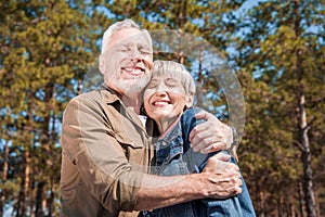 smiling senior couple of tourists embracing with closed eyes in sunny day.