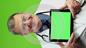 Smiling senior doctor holds digital tablet for medical news or advertising.