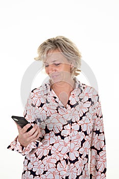 Smiling senior elderly woman looks at the screen of cell mobile phone in a black white blouse with pink flowers smartphone on