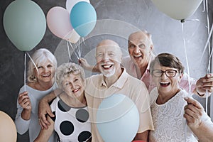 Smiling senior friends with colorful balloons enjoying meeting