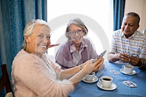 Smiling senior friends playing cards while having coffee