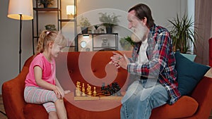 Smiling senior grandfather playing chess board game with teen granddaughter child girl kid at home