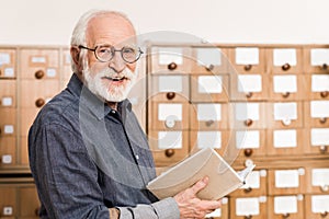 smiling senior male archivist holding book and looking photo