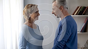 Smiling senior male and female standing and looking at each other, both happy