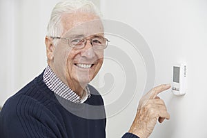 Smiling Senior Man Adjusting Central Heating Thermostat