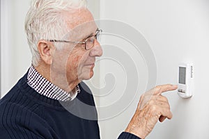 Smiling Senior Man Adjusting Central Heating Thermostat