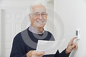 Smiling Senior Man With Bill Adjusting Central Heating Thermosta