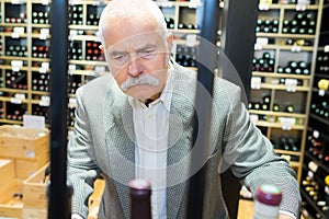 smiling senior man choosing wine bottle at liquor store