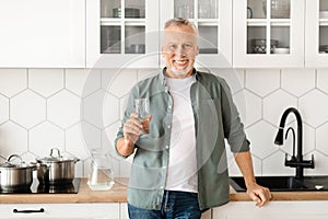 Smiling Senior Man With Glass Of Water In Hand Posing In Kitchen