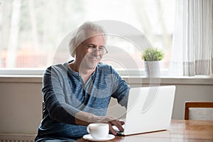 Smiling senior man in glasses working on laptop at home