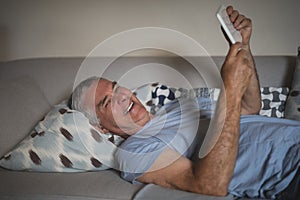 Smiling senior man holding digital tablet while lying on sofa at home