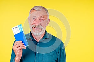 Smiling senior man holding passport in blue cover and tickets studio yellow background