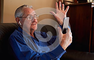 Smiling Senior Man At Home Waving As He Makes Video Call To Family On Mobile Phone