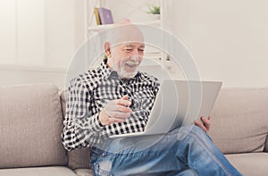 Smiling senior man reading news on laptop
