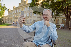 Smiling senior man, recovering male patient in wheelchair making a video call using smartphone while spending time alone
