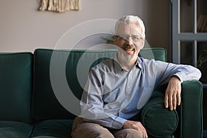 Smiling senior man sit on sofa in living room, portrait