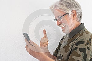 Smiling senior man standing against white background using smart phone in video call with family. Old people using new technology