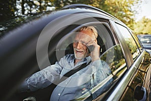 Smiling senior man talking on his cellphone in a car
