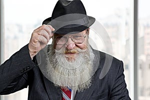 Smiling senior man touching his black hat and looking at camera.